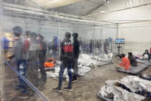 Image: Migrants crowd a room with walls of plastic sheeting at the U.S. Customs and Border Protection temporary processing center in Donna
