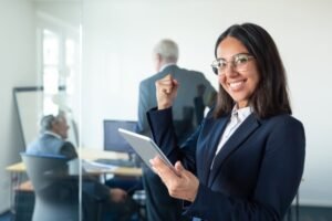 feliz-mujer-profesional-gafas-traje-sosteniendo-tableta-haciendo-gesto-ganador-mientras-dos-hombres-negocios-trabajan-detras-pared-vidrio-copie-espacio-concepto-comunicacion_74855-14248